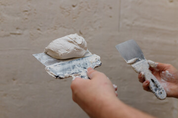Male hands with spatula using putty for wall, builder making overhaul.