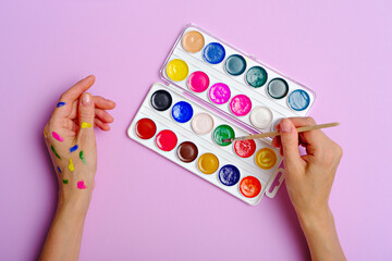 painted hands with brush and paints on lilac background, home creativity, novice artist