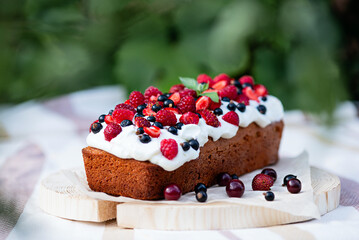 homemade delicious cake or cupcake with berries and whipped cream decorated with strawberries, raspberries, currants on wooden frame, summer snack in fresh air