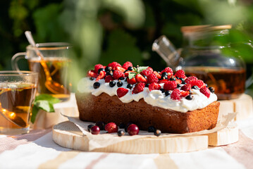 homemade cake or cupcake with berries and whipped cream decorated with strawberries, raspberries, currants on wooden board, summer tea drinking in fresh air