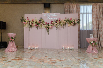 Upper part of pink decorative wedding arch, screen with flowers, just married names. Presidium with Mr. and Mrs. inscription. Decorations for wedding hall, festive party in restaurant.