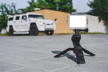 The mockup of the Action Camera stands on a tripod on paving slabs. Against the background of a white SUV car.
