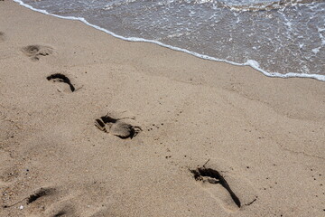 Footprints of a man on the yellow beach sand from walking barefoot by the sea with water that washes away the footprints.