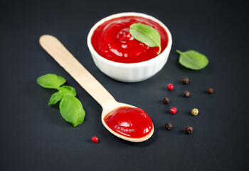 Bowl of ketchup and spoon of red tomato sauce on black kitchen table