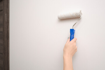 Painting works. A woman paints a light wall with a paint roller. Close-up on a hand with a tool. Construction worker, tool, apartment renovation.