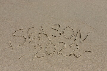 The inscription season 2022 on the sand by the water and the rising wave, seashore beach vacation by the sea