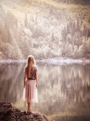 A woman looks into the distance standing on the edge of a stone near a clear forest lake. Nature reserve. Soft focus