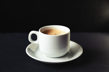 White cup of espresso coffee on a black background.