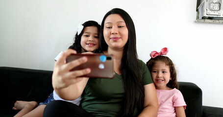 Obraz premium Asian mother taking selfie with two little daughters at home, holding smartphone