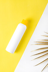 Body care product on yellow and white background with golden palm leaf. Unlabeled bottle of sunscreen cream or shower gel. Beauty mockup with copy space. Flat lay