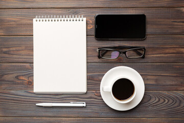 Modern office desk table with notebook, smartphone and other supplies with cup of coffee. Blank notebook page for you design. Top view, flat lay