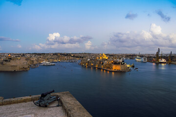 Fototapeta na wymiar Malta panorama of fortified Three Cities with moored ships and clouds above. Evening view of Vittoriosa, Senglea and Cospicua across the Grand Harbour, seen from Upper Barrakka Gardens in Valletta.
