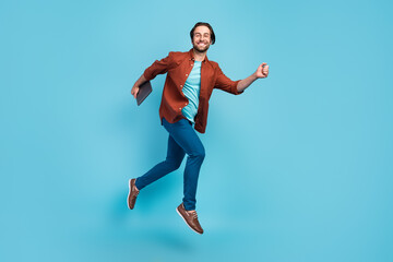 Fototapeta na wymiar Full lengh photo of funky brunet millennial guy run with laptop wear eyewear shirt trousers footwear isolated on blue background