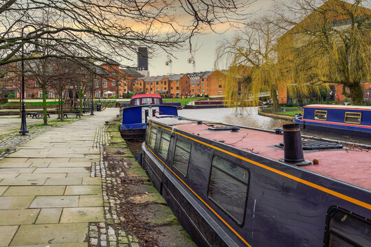 Manchester, UK moored narrow-boats at Castlefield Basin inner city conversation area. Day view of houseboats on Bridgewater Canal, before traditional low-rise buildings.