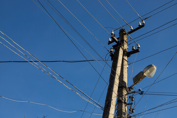Electric wires hanging on a pole with a lighting lamp photographed from below on a background of...