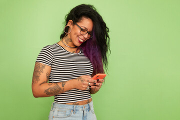 Studio shot of tattooed and pierced woman looking at smart phone