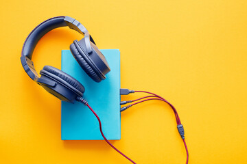 Book in a blue cover and black headphones on a bright yellow background, top view, close-up....