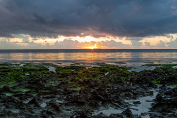 Panoramic view of the sunrise over the ocean. Stones with greenery ahead