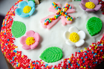 Traditional Easter cake decorated with icing and Easter decor: cross, flowers, leaves, dragee with molasses. Traditional sweets for the Christian holiday. Festive background.