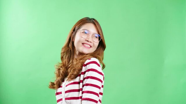 Cheerful young Asian woman with eyeglasses raising hands up, shaking and having fist pump from happiness, smiling woman face, green screen background.