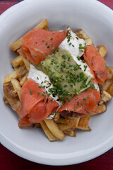Top view of french fries with smoked salmon, cream cheese and guacamole sauce in a white bowl on the red wooden table.