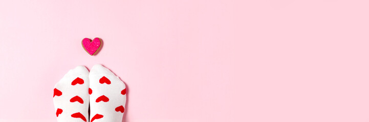 Banner with white socks and gingerbread in the shape of a flat lay. Stylish Valentine's Day celebration design with space for text. Top view of the feet on a pink background