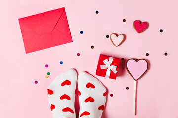 Red envelope, socks and sweet gingerbread for the holiday on a pink background. Bright socks and a red gift box with a flat lay bow. Romantic Valentine's Day Gifts