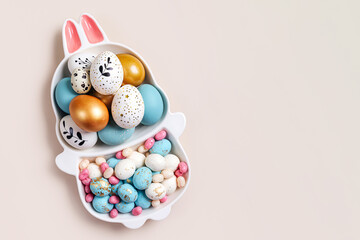 Happy Easter concept. Cute plate in the shape of a bunny with  Easter eggs and candy on beige background.