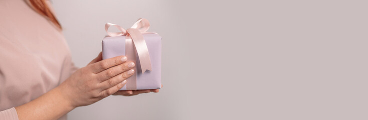 Woman hands holding surprise gift box present wrapped paper with pink ribbon on pastel background with copy space. 8 march, birthday, mother's day