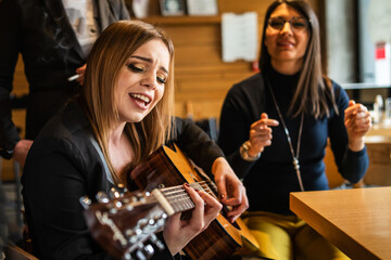 Front view portrait of adult caucasian woman sitting at cafe with guitar on her lap looking to the hand holding accord singing to her friends - female musician relaxed real people leisure concept