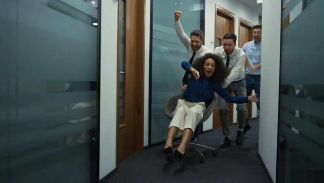 Happy employees group celebrating business success racing office chair indoors.