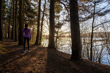 Female jogger standing in forest and looking at lake