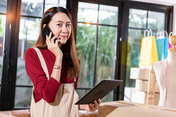 Young Asian shop owner woman calling to customer and checking stock on digital tablet at home. SME small business entrepreneur prepare for shipping product, online store e-commerce or service support