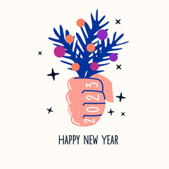 The hand holds a bouquet of fir branches with toys. Happy New Year 2023. New Year's greetings.