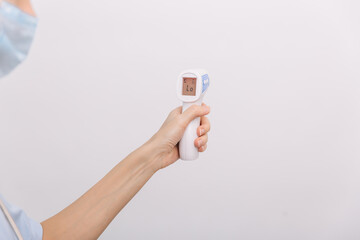 Temperature measurement gun in doctor hands. Close-up shot of doctor wearing protective surgical...