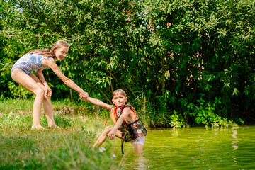 Blond preteen sister helps little brother out of the water. Summer, holiday, outdoor activities at summer time concept.