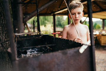 Obraz na płótnie Canvas Thoughtful preteen bare shoulder boy near the grill with sctic on hands in summer backyard of village house.