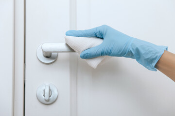 Naklejka premium Cleaning black door handles with an antiseptic wet wipe and blue gloves. Sanitize surfaces prevention in hospital and public spaces against corona virus. Woman hand using towel for cleaning.