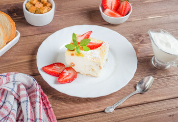 Cottage cheese casserole with fresh cream and strawberries on a white plate on a wooden background