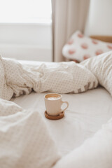 Fototapeta na wymiar Cozy unmade bed with a coffee cup in the morning, breakfast in bed