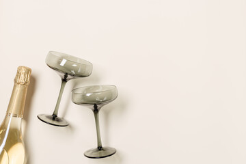 Champagne glasses tinted grey glass, Champagne or sparkling wine bottle on beige background. Festive drink concept, glare and sunlight. Modern wine colored glasses. Creative flat lay