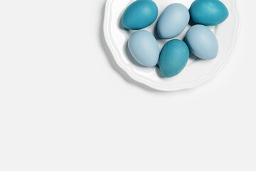 Painted Easter eggs blue gray colored on round white plate, light background with copy space. Chicken egg pastel shades. Easter holiday food, monochrome minimal design aesthetic flat lay