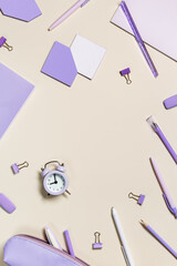 Frame with school stationery very peri trend color, pencils, pens, clips, alarm clock, pencil case. Back to school flat lay on beige background. Office supplies pastel colors on table