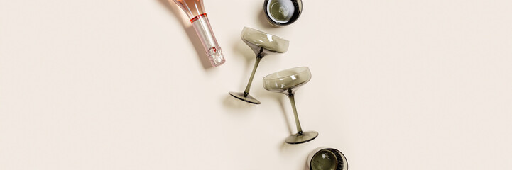 Rose champagne bottle and champagne glasses from tinted glass on beige background with copy space, banner. Summer drink minimal concept. Trendy vintage colored glass. Creative top view