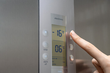 Close-up of a woman's hand regulates the temperature of the refrigerator freezer. Stylish modern grey refrigerator.Woman's hand raises the temperature to minus sixteen degrees