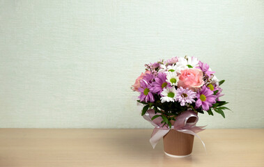 Fototapeta na wymiar A beautiful bouquet of flowers in a vase with a bow is on the table. Place for text