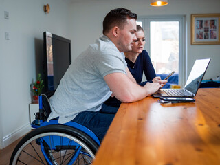 Man on wheelchair and woman looking at laptop at home