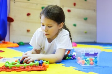 Fototapeta premium a child a girl on the floor of a children's rehabilitation center for correction collects a chain of viruses from a toy. the concept of lifestyle