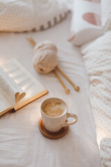 Cozy morning still life with a coffee cup, needles and a book with pages folded into a heart shape in bed