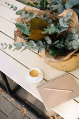 Delicious fresh morning espresso coffee cup standing on the wooden bench with a basket of eucalyptus and a paper notepad